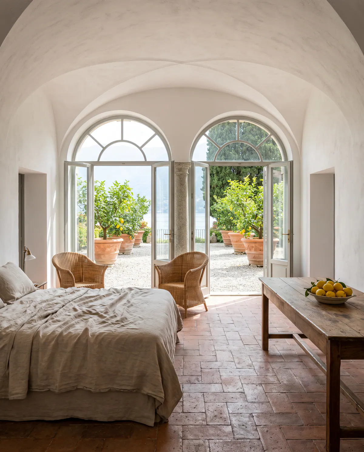 Suite Limonaia : chambre blanche voûtée, portes vitrées en arc ouvertes sur des citronniers en pots de terre cuite.