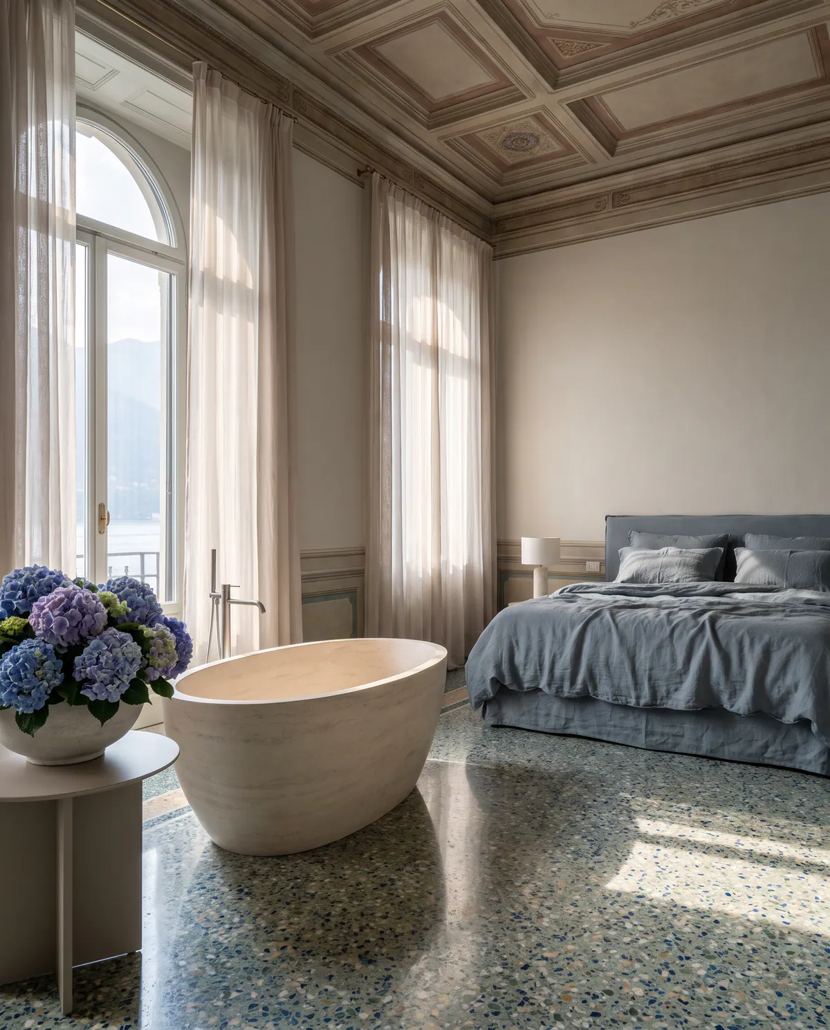 Suite Ortensia : baignoire en pierre près d’une haute fenêtre sur le lac, hortensias bleus.